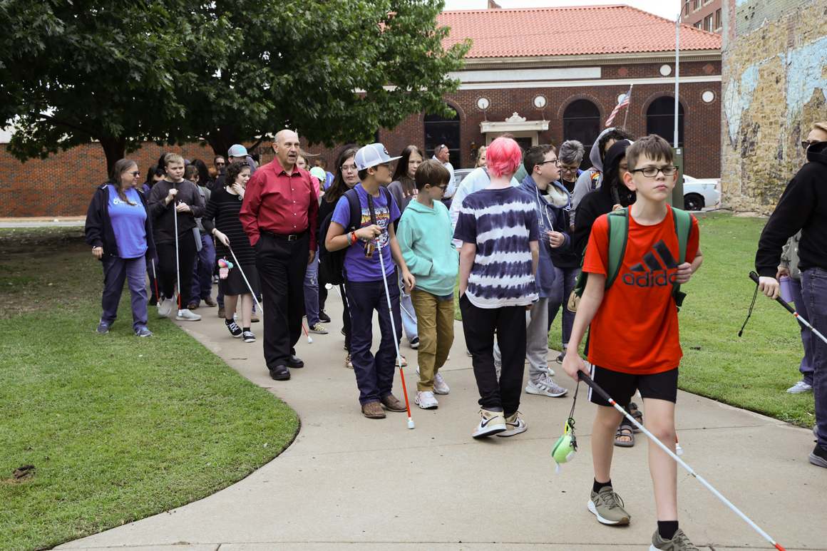 Students with white cane walking on the sidewalk.