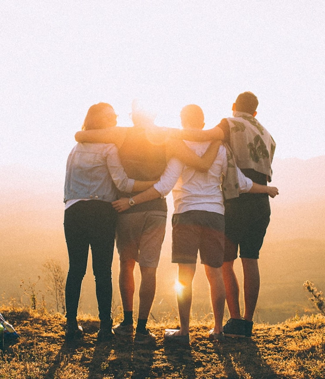 four person hands wrap around shoulders while looking at sunset