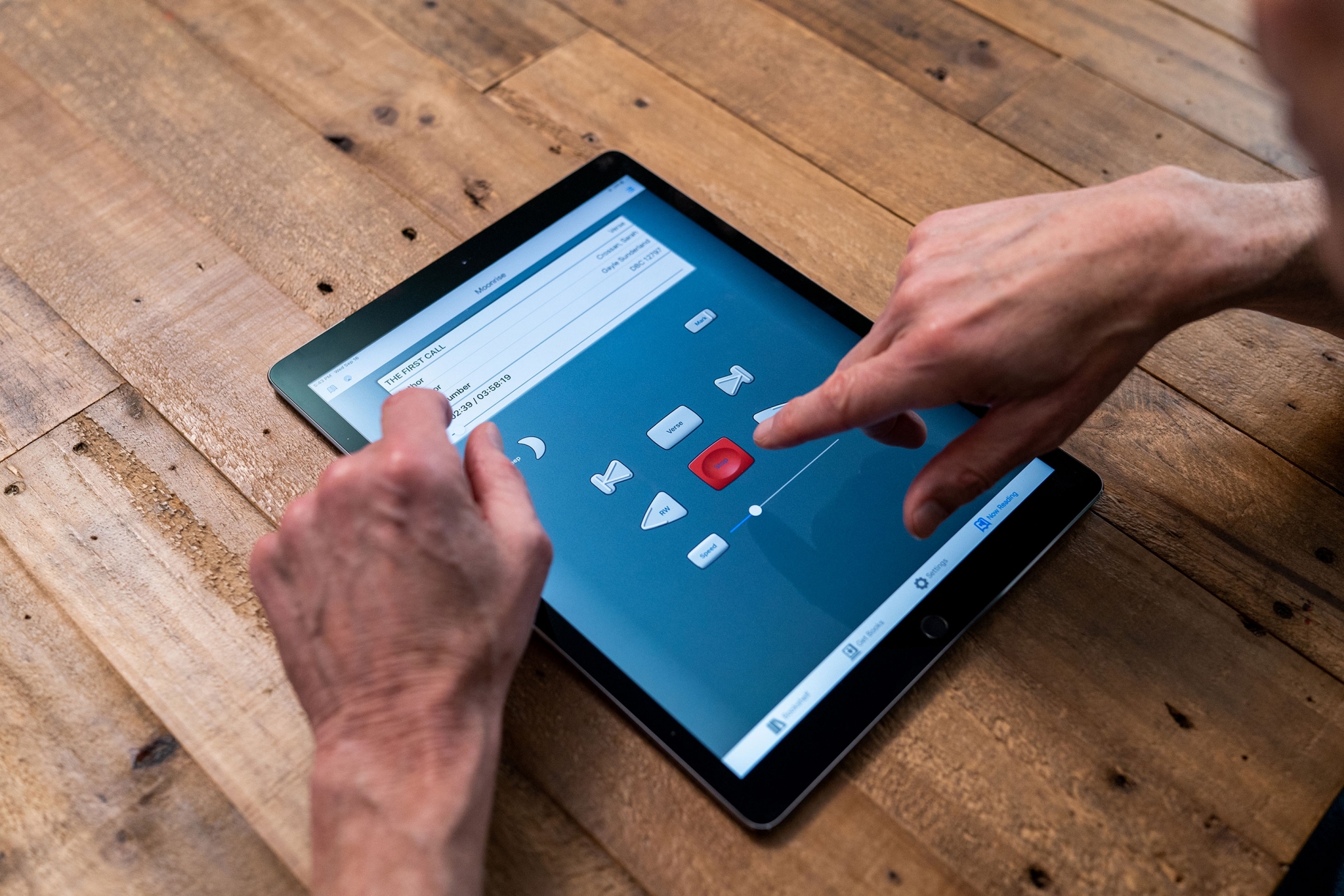 A closeup of a tablet, resting on a rough, wooden table, displaying the BARD mobile app. A hand reaches toward the play/stop button in the center of the screen. A closeup of a tablet, resting on a rough, wooden table, displaying the BARD mobile app. A hand reaches toward the play/stop button in the center of the screen.