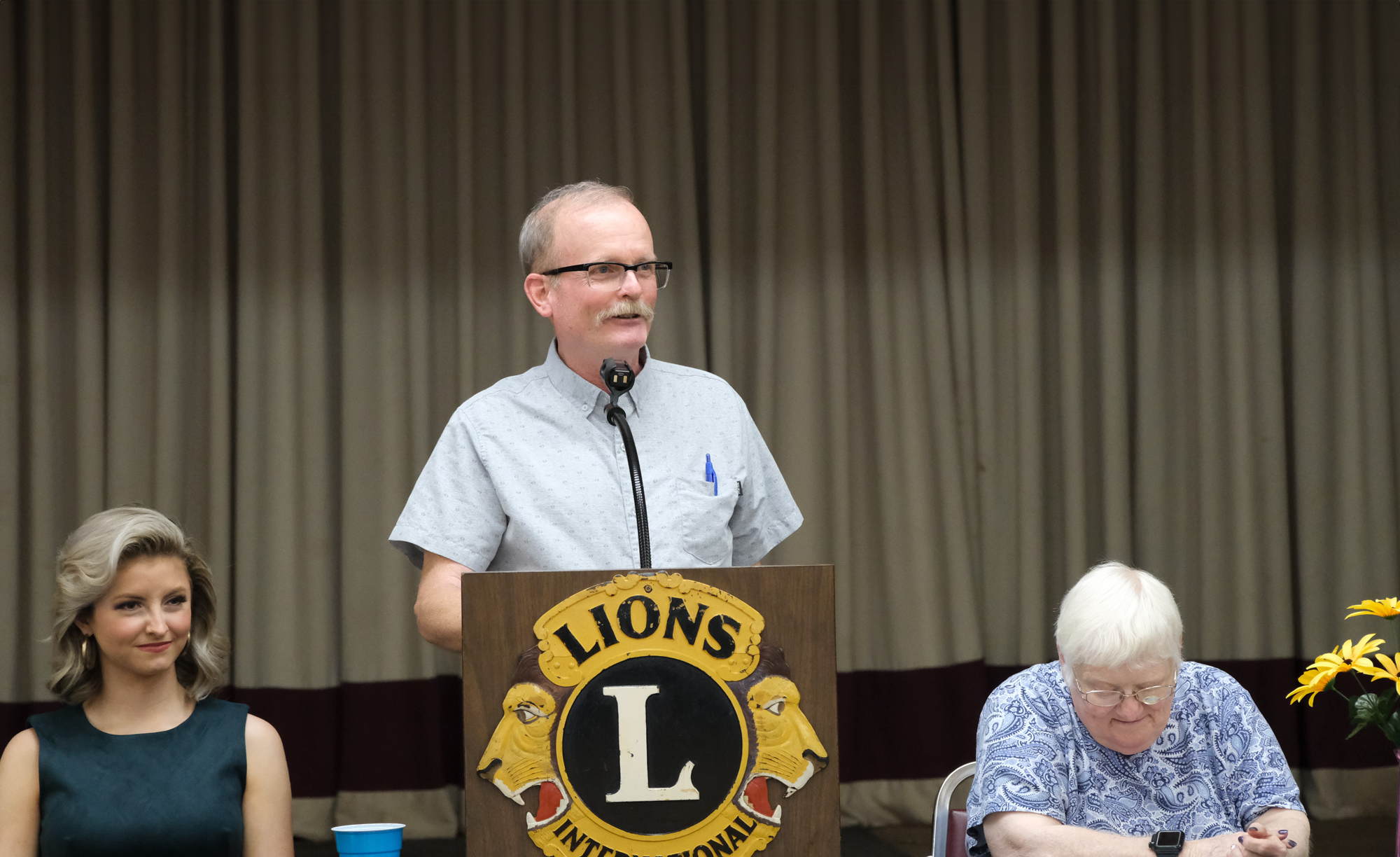 OLBPH Director Kevin Treese thanks the members of the OSLS for their support of the library and reports on library activities and changes. OLBPH Director Kevin Treese at the podium with a woman sitting to his right and a woman sitting to his left
