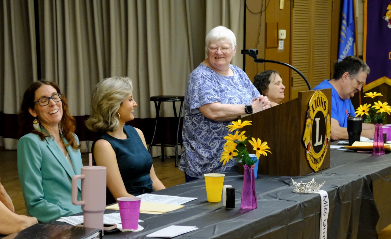OSLS President Julie Brantley at the podium and the two women at the  table laughing. 