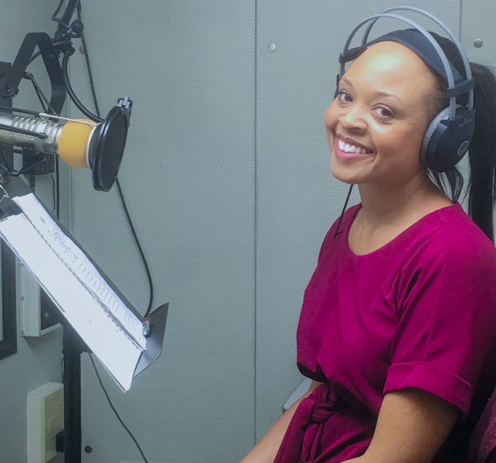 A woman in the studio in front of a mic and reading material.