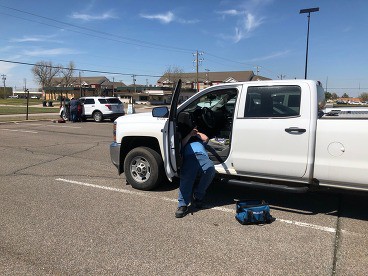 Worker installing automatic vehicle locator devices in a white pickup truck.