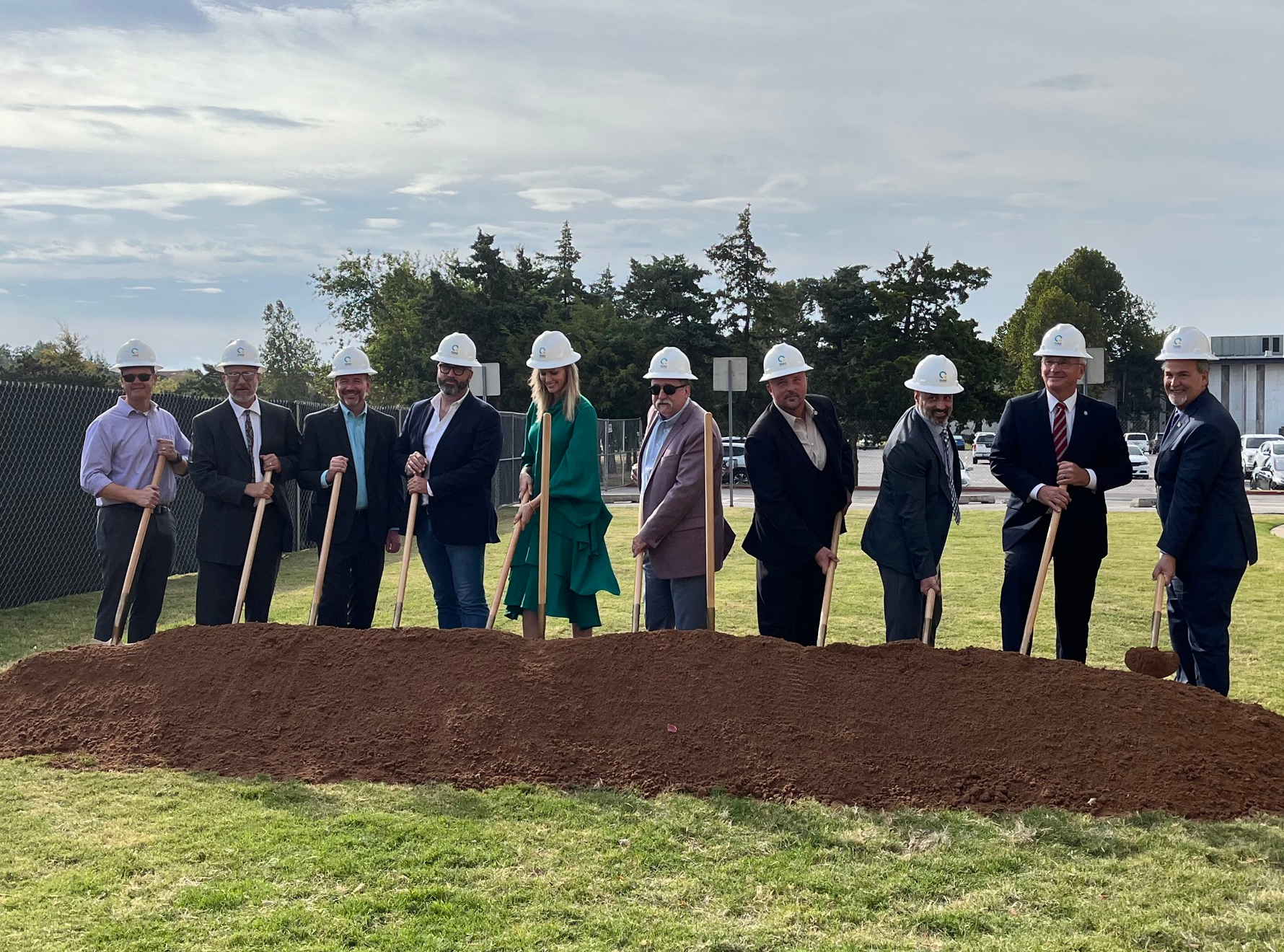 OMES and QUAD Construction stakeholders break ground using shovels and adorning hard hats.