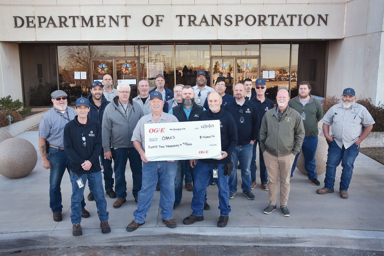 Facilities Management team members stand holding rebate check from OG&E in front of the Department of Transportation building.