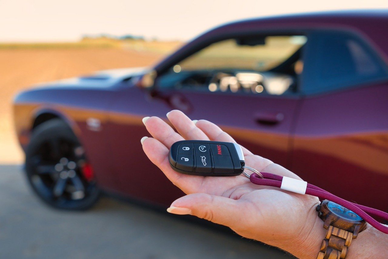 woman's hand holding a car fob with a car in background