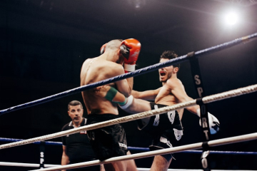 Kickboxer kicking a blocking opponent in a ring as a ref watches Kickboxer kicking a blocking opponent in a ring as a ref watches