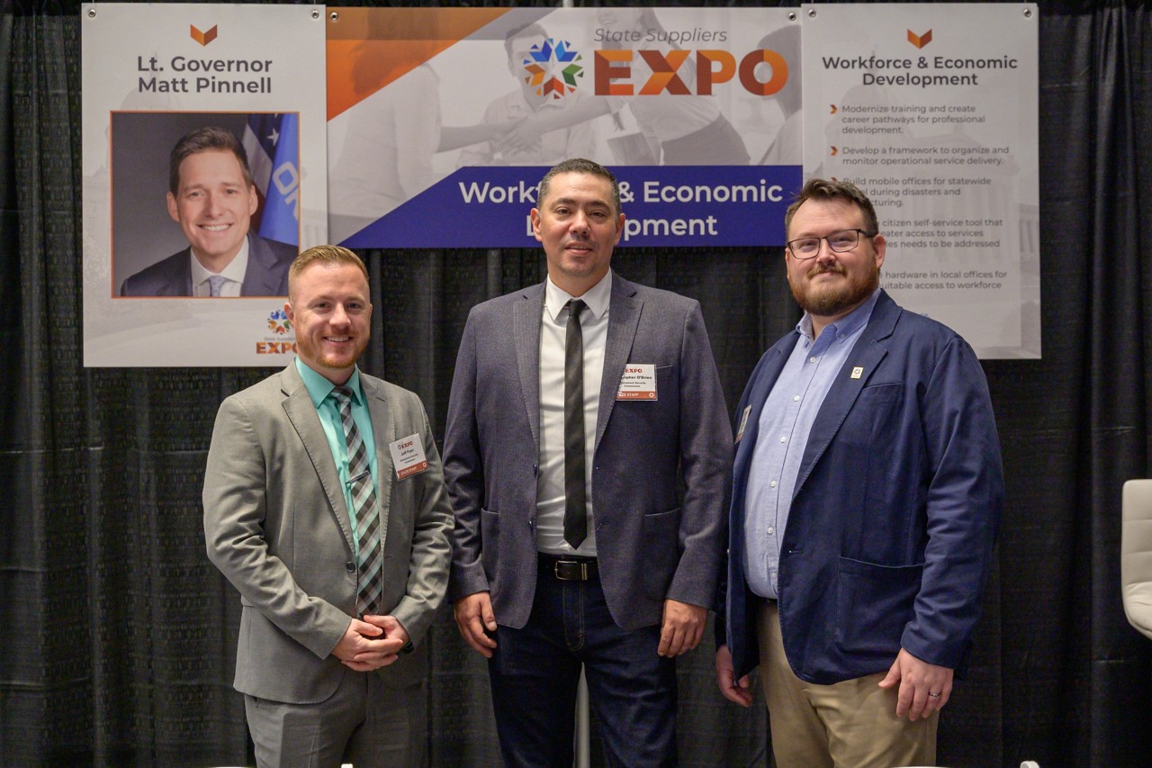 Three cabinet staff smile in front of the Workforce and Economic Development booth.