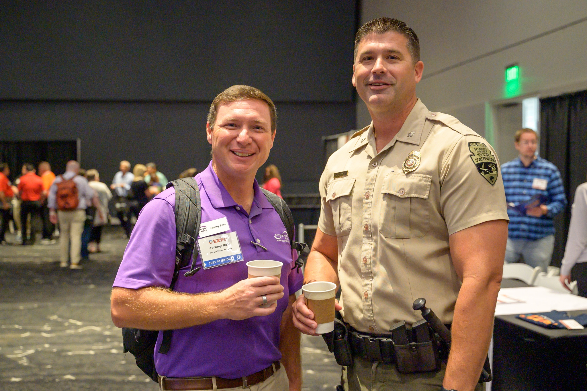 Wildlife Conservation game warden smiling and holding coffee with an attendee.