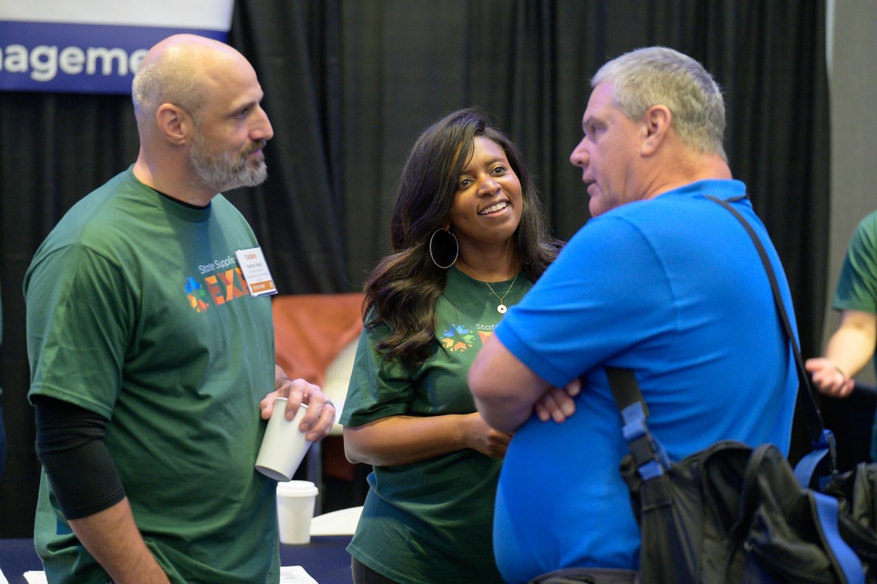 Two state employees  visit with an attendees in the OKC Convention Center ballroom during the 2024 State Suppliers Expo.