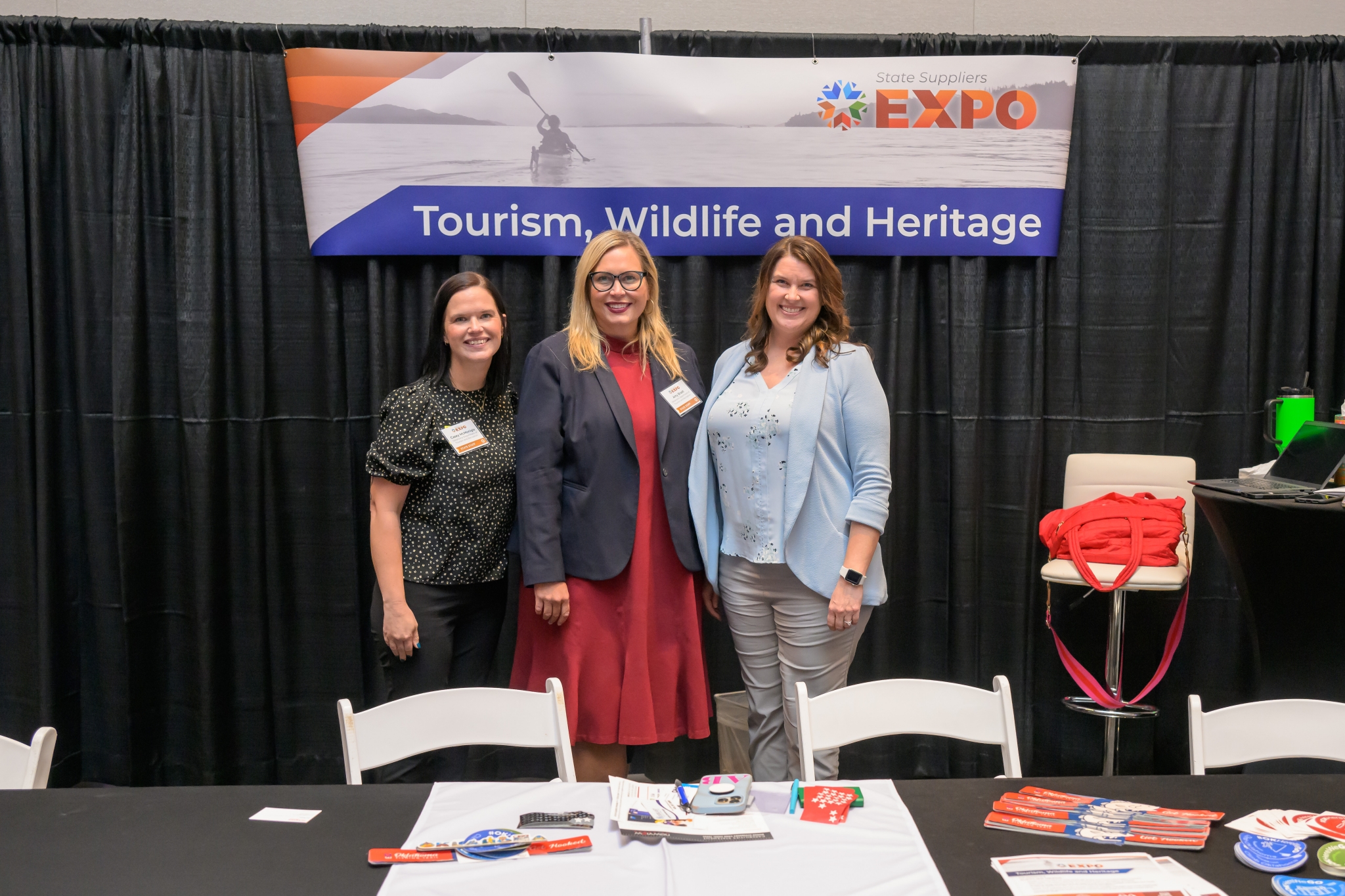 Three state staff members stand smiling at the Tourism, Wildlife and Heritage booth