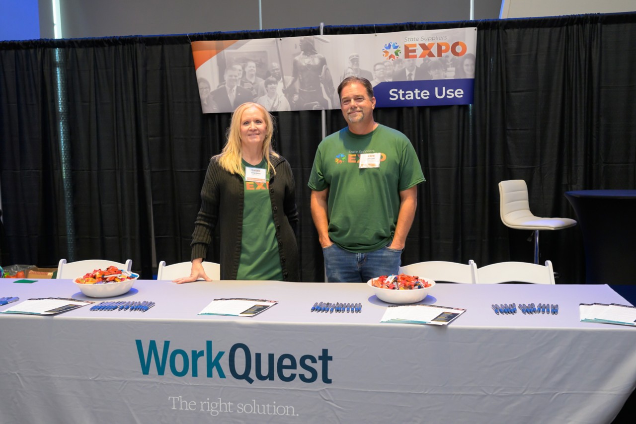 Two state staff members smile while standing at the State Use booth