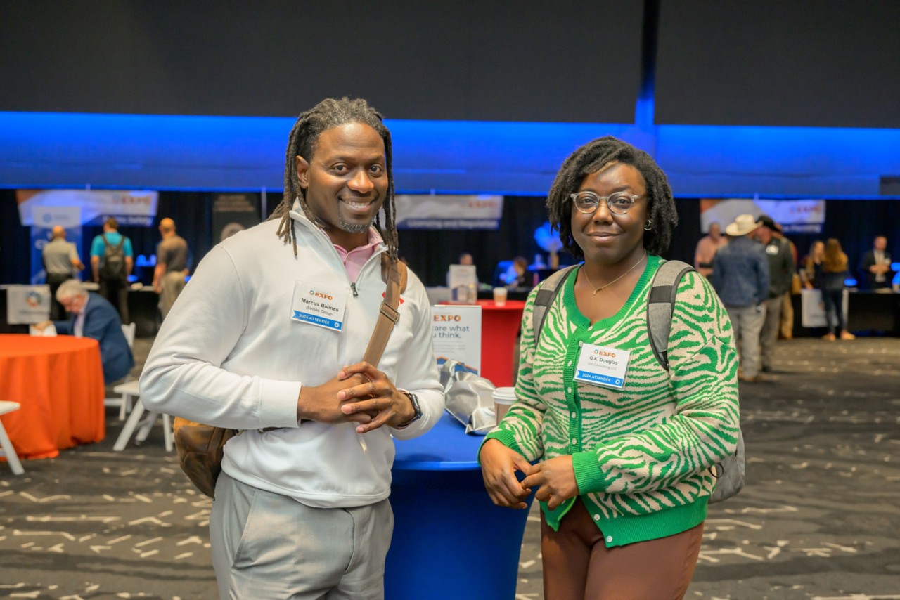 Two attendees smiling by a bistro table