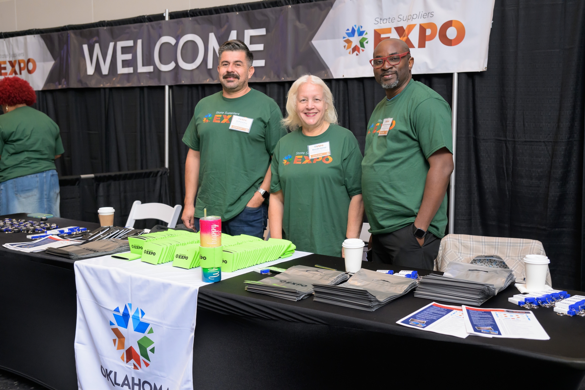 Three state staff members stand smiling at the welcome booth